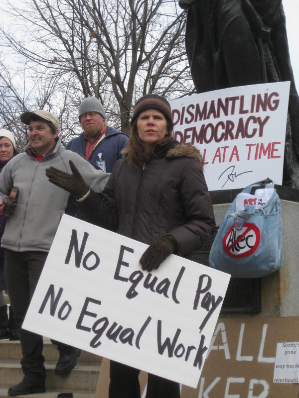 Rep. Taylor speaking to crowd with sign saying "no equal pay, no equal work"